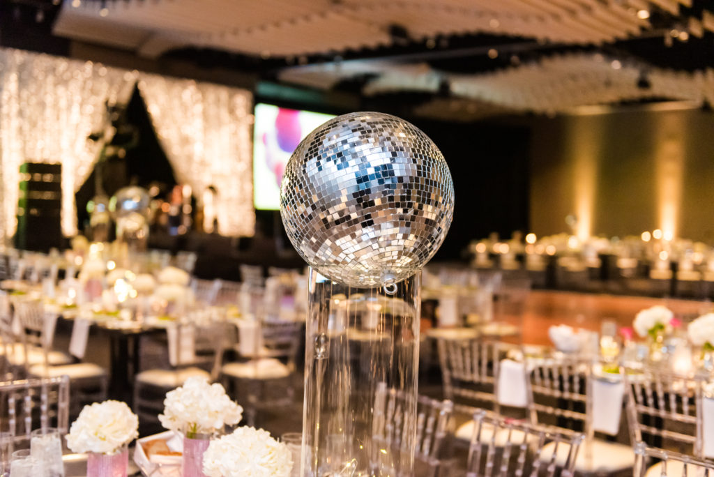 Disco ball on top of a hurricane vase in a ballroom. 